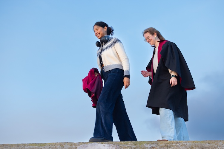 Two postgraduate students take part in the traditional Pier Walk in St Andrews, walking together beneath a clear blue sky.